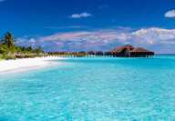 Vista de una playa en las Maldivas con un hotel sobre pilotes sobre aguas turquesas