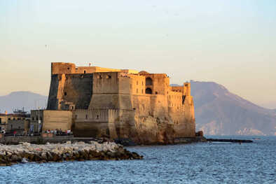 Paesaggio del golfo di Napoli in Italia con un castello medievale in primo piano, un punto di riferimento della città, di fronte alle montagne in lontananza, una bella giornata con tempo perfetto all'ora del tramonto
