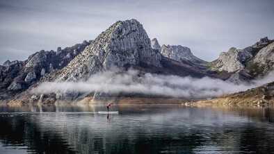 Una chica o mujer con abrigo rosa practica paddle surf explorando en un lago de montaña con niebla Una chica o mujer con abrigo rosa practica paddle surf explorando en un lago de montaña con niebla