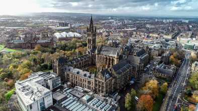 Imagen aérea de bajo nivel sobre el follaje otoñal de los árboles en Kelvingrove Park, Glasgow, hasta la torre gótica de la Universidad de Glasgow con el paisaje urbano detrás. Imagen aérea de bajo nivel sobre el follaje otoñal de los árboles en Kelvingrove Park, Glasgow, hasta la torre gótica de la Universidad de Glasgow con el paisaje urbano detrás.