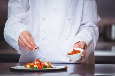 Un chef espolvoreando especias en un plato en una cocina comercial Un chef espolvoreando especias en un plato en una cocina comercial