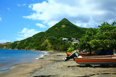 primera línea de playa de la isla de Martinica. Barco de pescador amarrado. Montañas verdes al fondo.